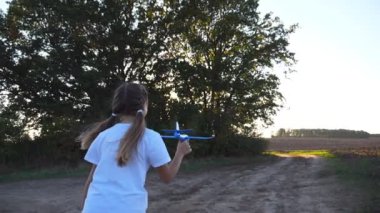 Sevimli küçük çocuk kır yolunda koşarken oyuncak uçak tutuyor. Yaz günü uçakla koşan mutlu küçük kız. Tasasız çocuk doğayla eğleniyor. Çocukluk hayali konsepti. Arka görünüm.