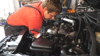 Tamirci oto servisinde araba bakımı yapıyor. Profesyonel tamirci atölyede otomobil motorunu kontrol ediyor. Garajda kaputun altında çalışan bir adam. Otomobil tanısı konsepti. Yavaş çekim.