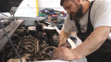 Tamirci arabanın motorunu tamir ediyor ve araba servisinde telefonla konuşuyor. Tamirci aracın kaputu altında çalışıyor ve iş arkadaşlarıyla görüşüyor. Otomobil motorunu kontrol et. Bakım ve tanı kavramı