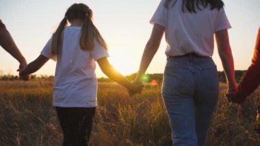 Happy family with small kids walks through grass field holding hands of each other at sunset. Mother and father with two little children going among meadow and enjoy to spending time together. Slow mo