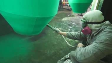 İşçi boya odasındaki detaylara yeşil boya püskürtüyor. Sanayi imalatında çalışan bir ressam. Uzman atölyede usta boya detayı. Üretimde parçaları boyayan adam. Yavaş çekim. Yakın çekim.