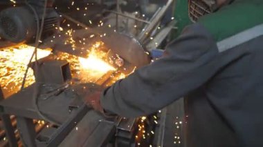 Güvenlik koruması altında çalışan işçiler metal kesmek için testere kullanıyor. Garajda çeliği kesen dairesel testereli bir adam. Metal öğüten adam. Endüstriyel üretim. Sıcak metalden kıvılcımlar çıkıyor. Dolly vurdu..