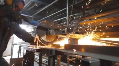 Atölyede çeliği kesen dairesel testereli sanayi işçisi. Güvenlik koruması altındaki adam metal kesmek için testere kullanıyor. Zanaatkar metali öğütüyor. Sıcak metalden kıvılcımlar çıkıyor. Yavaş çekim.