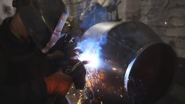 Endüstriyel üretimde koruyucu maske kaynak işçisi. Kaynakçı, metal fabrikasında iki çelik detayı arasında bağlantı kuruyor. Metal kaynak yapan adam. Yavaşça kapat..