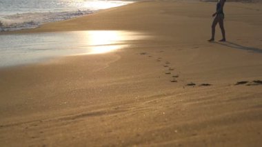 Gün batımında ıslak kumun üzerinden okyanusa giden mayolu güzel, ince bir kız. Mayolu genç bir kadın yüzmek için denize giriyor. Yaz tatilinde ya da tatilde iyi istirahatler. Yavaş çekim.
