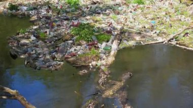 Nehir birçok plastik şişeyle kirlidir. Pek çok çöp doğadaki açık ve serbestçe ulaşılabilir yerlere atılır. Küresel çevre kirliliği sorunu. Ekolojik felaket kavramı.