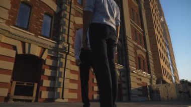 Genç erkek iş arkadaşları şehirdeki ofis binasının yanında konuşuyorlar. Kendine güvenen iş adamları gelecekteki açık hava projesinden bahsediyorlar. Meslektaşların iletişimi. İş ve finans kavramı. Dolly vurdu..