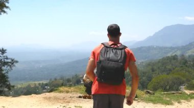 Sırt çantalı genç adam dağın tepesine ulaşıp ellerini kaldırdı. Erkek turist güzel bir kanyonun kenarında duruyor ve muzaffer bir şekilde kollarını kaldırıyor. Yavaş çekim Arka plan Görünümü Kapat.