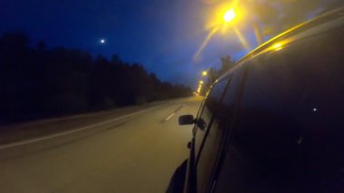 Geceleri kırsal yolda yarışan siyah jipin görüntüsü. Akşamları otomobille yola çıkıyoruz. Araç otoyol boyunca kırsal alanlardan hızla geçiyor. Trip ya da seyahat konsepti. POV.