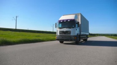 Kamera, yaz günü kargo karavanıyla otobanda mal taşıyan kamyonu takip ediyor. Arka planda doğa manzarası olan beyaz bir kamyon. Yavaş çekim ön görünümü