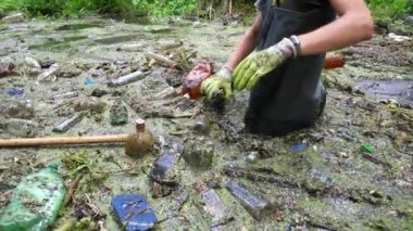 Kirli gölde enkaz toplayan kauçuk giysili tanınmayan çevreci aktivist. Koruyucu eldivenlerle çöpleri temizleyen gönüllü erkeklerin elleri. Çevre kirliliği koruması kavramı.