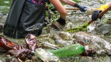 Koruyucu eldivenli kadın çevrecilerin elleri enkaz nehirlerini temizliyor. Kirli gölde plastik şişe toplayan kauçuk elbiseli tanınmayan gönüllüler. Çevre kirliliği koruması.