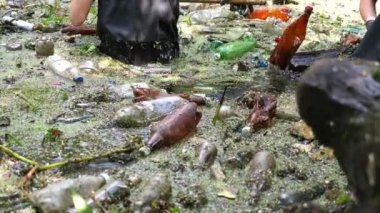 Koruyucu eldivenli kadın çevrecilerin elleri enkaz nehirlerini temizliyor. Kirli gölde plastik şişe toplayan kauçuk elbiseli tanınmayan gönüllüler. Çevre kirliliği koruması.