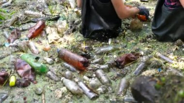 Koruyucu eldivenli kadın çevrecilerin elleri enkaz nehirlerini temizliyor. Kirli gölde plastik şişe toplayan kauçuk elbiseli tanınmayan gönüllüler. Çevre kirliliği koruması.
