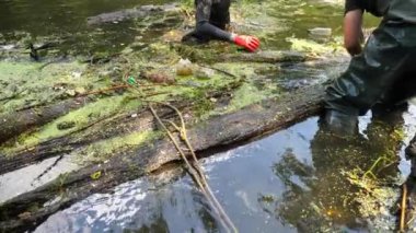 Kauçuk giysiler içinde tanınmayan erkek çevreciler kirli gölde enkaz topluyorlar. Koruyucu eldivenlerle pis nehri temizleyen gönüllüler. Çevre kirliliği koruması kavramı. Yavaş çekim