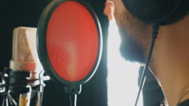 Ses stüdyosunda tanınmayan bir şarkıcı şarkı söylüyor. Adam yeni şarkı kaydediyor. Sakallı adam mikrofona şarkı söylüyor. Yaratıcı bir müzisyenin çalışması. Gösteri dünyası konsepti. Yan Görünüm Yavaş çekim Kapat.