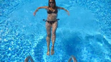 Güneş gözlüklü çekici kadın otel havuzunda yüzüyor. Genç kız sıcak ve güneşli bir günde havuzda ferahlatıcı yaz tatilinin tadını çıkarıyor. Bayan dinleniyor. Yavaş çekim Üst Görünüm.