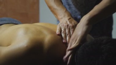 Male arms of masseur massaging shoulders of muscular sportsman in salon. Hands of professional massagist doing healing rubdown of back to young athlete in parlor. Concept of skincare. Slow motion.