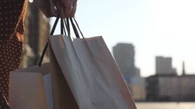 Alışveriş yaptıktan sonra alışveriş torbaları taşıyan genç bir kadın var. Kadın kolu, şehir caddesinde yürürken dolu kâğıt paketler tutuyor. Mevsimsel satış kavramı. Yavaş çekim.