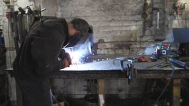 Kaynakçı, metal fabrikasında iki çelik detayı arasında bağlantı kuruyor. Endüstriyel üretimde koruyucu maske kaynak işçisi. Metal kaynak yapan adam. Yavaşça kapat..