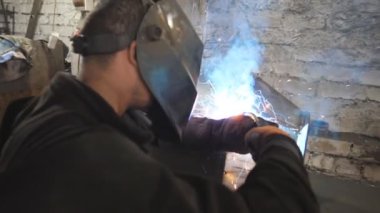 Kaynakçı, metal fabrikasında iki çelik detayı arasında bağlantı kuruyor. Endüstriyel üretimde koruyucu maske kaynak işçisi. Metal kaynak yapan adam. Yavaşça kapat..
