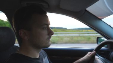 Araba kullanan genç bir adamın profili. Akşam vakti araba kullanan yakışıklı bir adam. Beyaz çocuk aracının içinde. Kuaförden yan görüntü. Yavaş çekim. Yakın çekim.