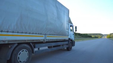 Akşamları otoyolda giden bir kamyonu takip ediyor. Kamyon arka planda güzel bir manzarayla kırsal alanda ilerliyor. Asfaltta kamyon gezintisi. Yan Görünüm Kapat.