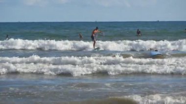 Mavi okyanus dalgasında kürek çeken ve güneşli bir günde sörf yapmayı öğrenen genç atletik adamı yakından takip edin. Denizde sörf tahtasında sörf yapan bir sporcu. Arka planda güzel bir deniz manzarası. Tatil kavramı