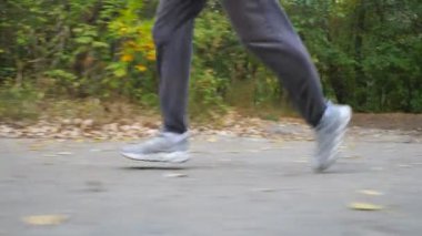 Sonbaharın başlarında ormanın yakınında yol boyunca koşan sportif bir adamın erkek ayakları. Genç atletin bacakları doğada patikaboyunca hızlı koşuyor. Dışarıda koşan güçlü bir adam. Sağlıklı aktif yaşam tarzı. Düşük görünüm.