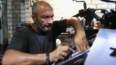 Profesyonel tamirci işyerinde motosiklet tamirciliği yapıyor. Erkek tamirci atölyede moto tamir ediyor. Garajda araba tamir eden yetişkin bir tamirci. Bakım hizmeti kavramı.