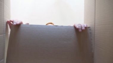 Çocuk hediyeyle kutuyu açıyor ve onu almak için elini çekiyor. Küçük çocuk duygu ve duygularla dolu bir kutuya bakar. Yüzünde neşe ve şaşkınlık ifadesi olan genç bir çocuk. Alt görünüm Yavaş çekim.