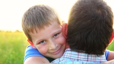 Kırsal kesimde küçük mutlu oğlunun elini tutan genç bir baba. Küçük gülümseyen çocuk kameraya bakıyor ve arka planda parlak güneş ışığına karşı babasına sarılıyor. Aile dinlenmesi kavramı. Kapat..