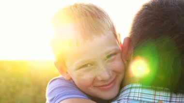 Kırsal kesimde küçük mutlu oğlunun elini tutan genç bir baba. Küçük gülümseyen çocuk kameraya bakıyor ve arka planda parlak güneş ışığına karşı babasına sarılıyor. Aile dinlenmesi kavramı. Kapat..