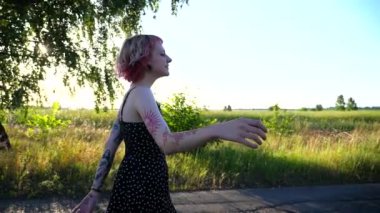 Siyah elbiseli kaygısız hippi kadın kırsalda boş bir yolda yürüyor. Pembe saçlı mutlu punk kızı, kır yolunda gezerken aylak aylak dolaşıyor. Genç bayan hippi dışarıda eğleniyor..