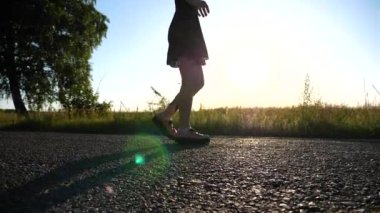 Hipster 'ın kadın bacakları kırsaldaki boş asfalt yolda yürüyor. Yaz günü kırsala giden hippi kadın dövmesi yaptırmış. Arka planda güzel manzaralı bir manzara. Yavaş çekim.