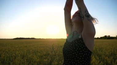 Mutlu punk kızı gün batımında yeşil buğday tarlasında pembe saçlarıyla oynuyor. Kulak tünelleri olan gülümseyen bayan hippi arpa otlağında eğleniyor. Tasasız hippi kadın doğada vakit geçirmekten hoşlanıyor..