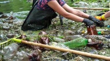 Koruyucu eldivenli kadın çevrecilerin elleri enkaz nehirlerini temizliyor. Kirli gölde plastik şişe toplayan kauçuk elbiseli tanınmayan gönüllüler. Çevre kirliliği koruması.