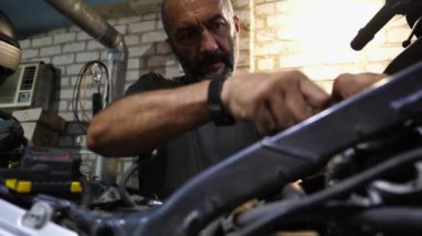 Erkek tamirci, motorun motorunu tamir etmek için işyerindeki aleti kullanıyor. Profesyonel tamirci atölyede motosiklet tamir ediyor. Garajda çalışan yetişkin bir tamirci. Bakım hizmeti kavramı.