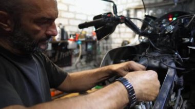Erkek tamirci, motorun motorunu tamir etmek için işyerindeki aleti kullanıyor. Profesyonel tamirci atölyede motosiklet tamir ediyor. Garajda çalışan yetişkin bir tamirci. Bakım hizmeti kavramı.