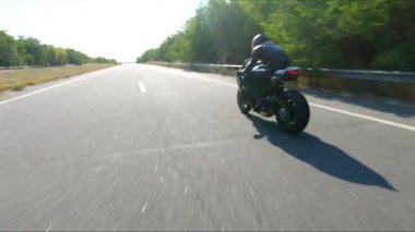 Anayolda motosiklet süren motosikletliyi takip edin. Motosikletli, kır yolunda motosikletiyle yarışıyor. Yolculuk sırasında bisiklet süren adam. Yolculukta özgürlük ve macera kavramı. Hava görüntüsü.