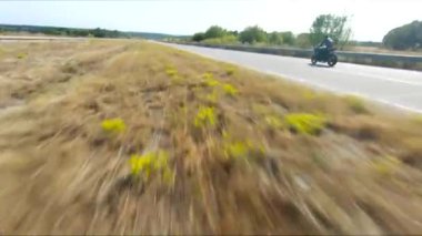 Anayolda motosiklet süren motosikletliyi takip edin. Motosikletli, kır yolunda motosikletiyle yarışıyor. Yolculuk sırasında bisiklet süren adam. Yolculukta özgürlük ve macera kavramı. Hava görüntüsü.