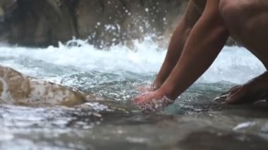 Unrecognizable hiker washing hands in mountain river with clear cool water. Guy standing among river with fast stream and refreshing. Male tourist during his travelling. Slow mo Low view Close up.