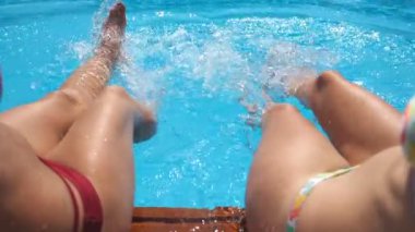 Otelin havuzunda kristal berrak su sıçratan dişi bacaklar. Havzanın kenarında oturan iki arkadaş güneşli bir günde tatilin tadını çıkarıyorlar. Yaz tatili ya da tatil kavramı. Yavaş çekim bakış açısı.