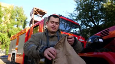 Erkek itfaiyeci, büyük kırmızı bir arabanın arka planına kask ve kar maskesi takıyor. İtfaiye arabasının yanında tam teçhizatlı genç itfaiyeci çalışmaya hazır. Hayat kurtarma kavramı ve kahramanlık mesleği.