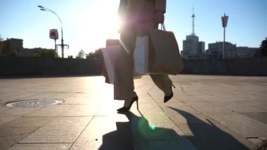 Genç kız şehir caddesinde yürüyen kağıt paketler taşıyor. Güzel bir kadın alışveriş sonrası alışveriş çantalarını şehir meydanında tutuyor. Satış ve indirim kavramı. Düşük görünüm Yavaş çekim Yakın çekim.