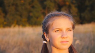 Güzel bir akşam gün batımına bakan ve parlak güneş ışınlarıyla aydınlanan küçük tatlı bir kızın portresi. Güzel bayan çocuk doğada vakit geçiriyor. Tasasız ve özgür olma kavramı. Dolly vurdu.