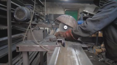 Güvenlik koruması altında çalışan işçiler metal kesmek için testere kullanıyor. Garajda çeliği kesen dairesel testereli bir adam. Metal öğüten adam. Endüstriyel üretim. Sıcak metalden kıvılcımlar çıkıyor. Dolly vurdu..