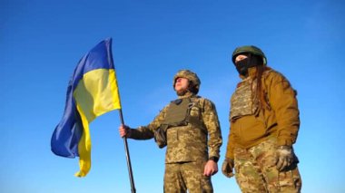 Ukrayna bayrağı sallayan Ukrayna ordusunun askerleri. Üniformalı askerler mavi gökyüzüne bayrak kaldırdı. Rus saldırısına karşı zafer. İstila direnci konsepti. Yavaş çekim.