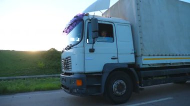 Kargo karavanıyla otoyolda gidip malları taşıyan kamyoneti kapatın. Kamyon gün batımında kırsalda hızla ilerliyor. Kargo taşıma konsepti. Güzel arka plan. Ağır çekim kenar görünümü