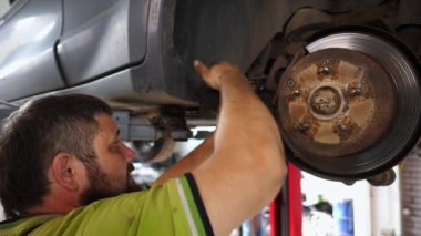 Üniformalı araba tamircisi atölyede ingiliz anahtarı kullanarak araba tamiri yapıyor. Yetişkin erkek tamirci garajdaki bir kaldırma aracının altında çalışıyor. Otomobil bakımı kavramı.